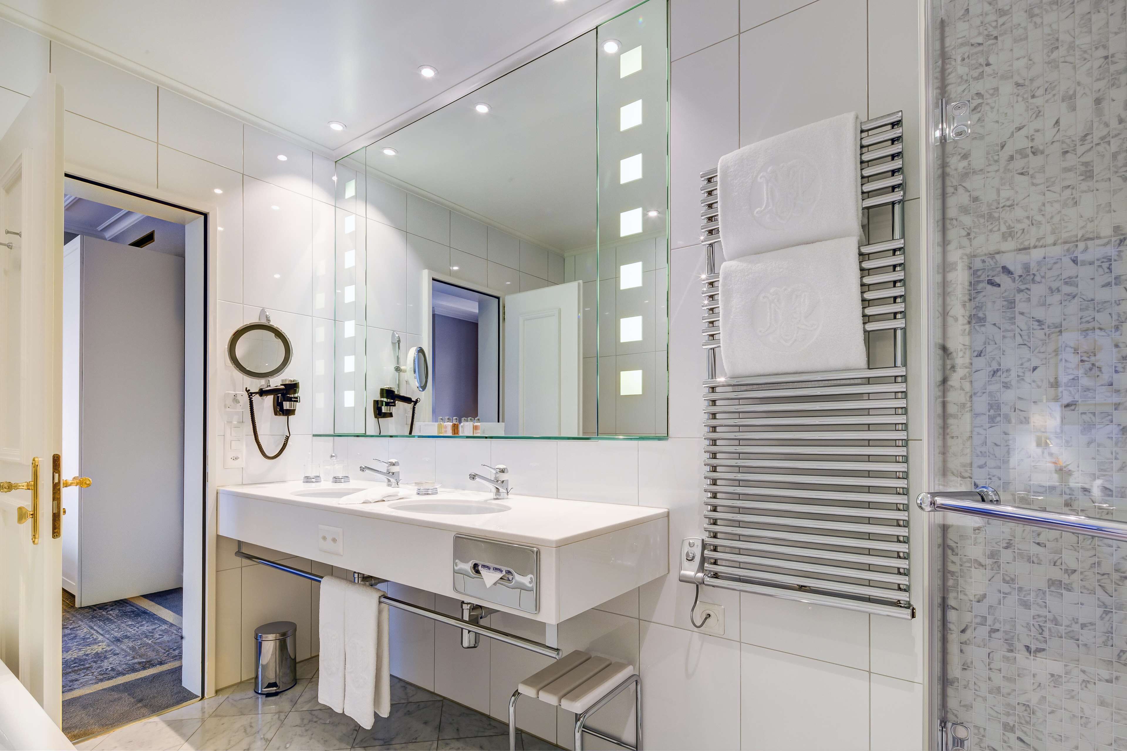 Une salle de bain moderne dotée d’un grand miroir, de deux vasques, d’un porte-serviettes et d’une cabine de douche en verre.