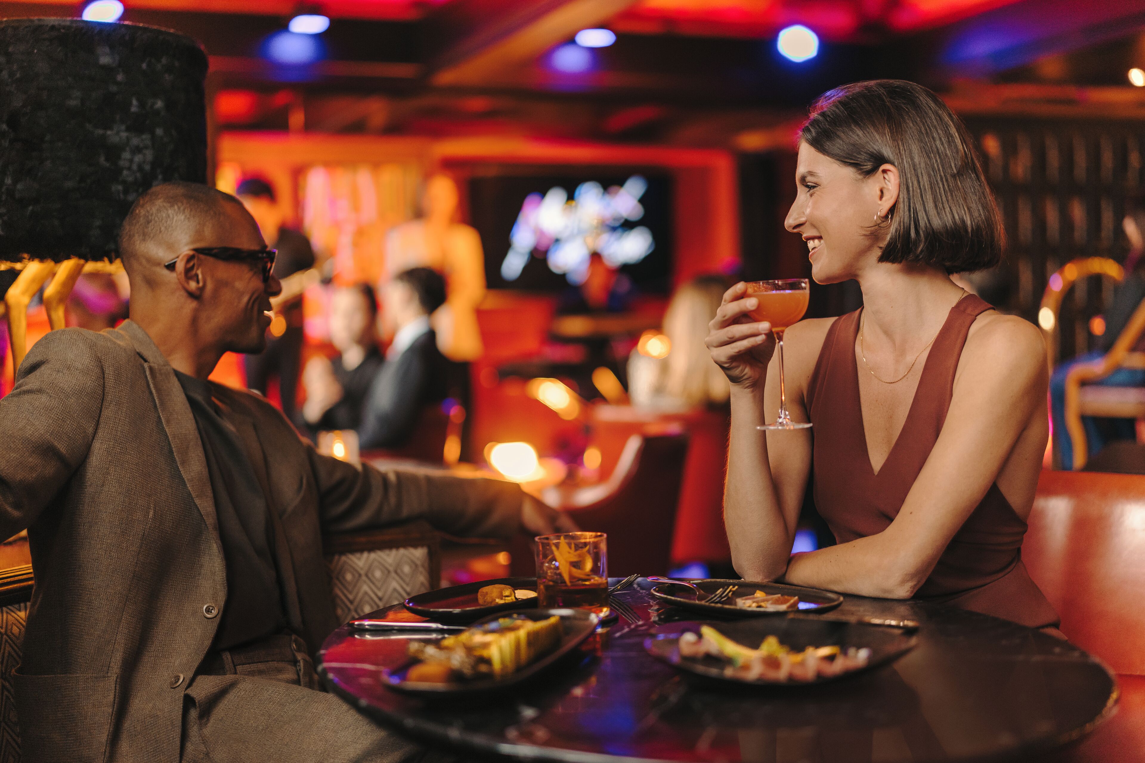 A couple seated at a table in a dimly lit bar with a television in the background.