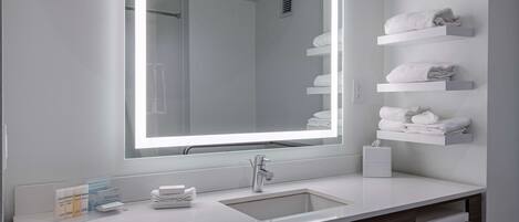 Un baño moderno con un espejo grande, lavamanos blanco y barras para toallas.