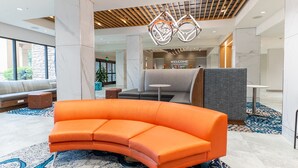 A modern lobby with a curved orange sofa, a wooden ceiling, and a 'WELCOME THE VOLUNTEER' sign. - Hampton Inn Knoxville-West At Cedar Bluff (Knoxville)