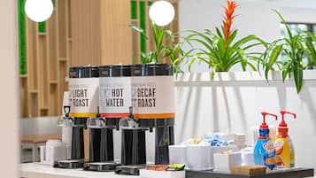 Una estación de café con tres dispensadores etiquetados 'Light Roast', 'Hot Water' y 'Decaf Roast'. También hay dispensadores de leche para café, así como una pequeña selección de aperitivos y condimentos en la encimera.