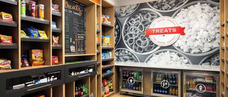 Una sección de aperitivos y bebidas con estantes llenos de diferentes productos, y dos refrigeradores para bebidas.
