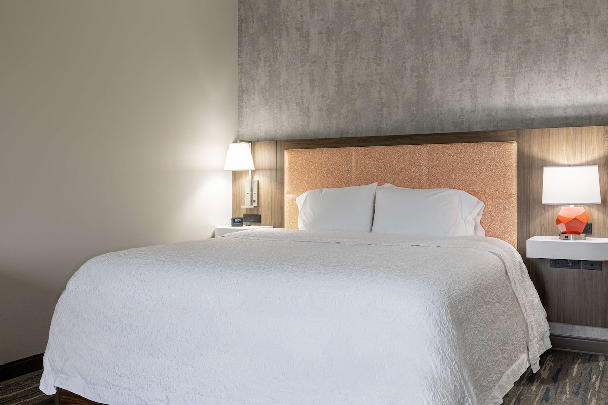 Una habitación de hotel con una cama grande, una mesita de noche con lámpara y un reloj de pared.
