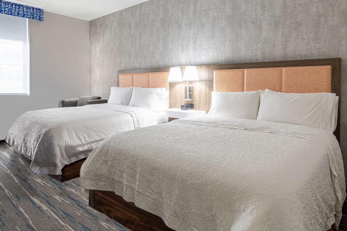 Una habitación de hotel con dos camas, un ventanal grande y una pared con textura.