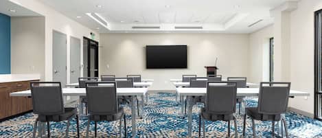 A conference room with a large table, chairs, a flat-screen TV, and a patterned carpet.