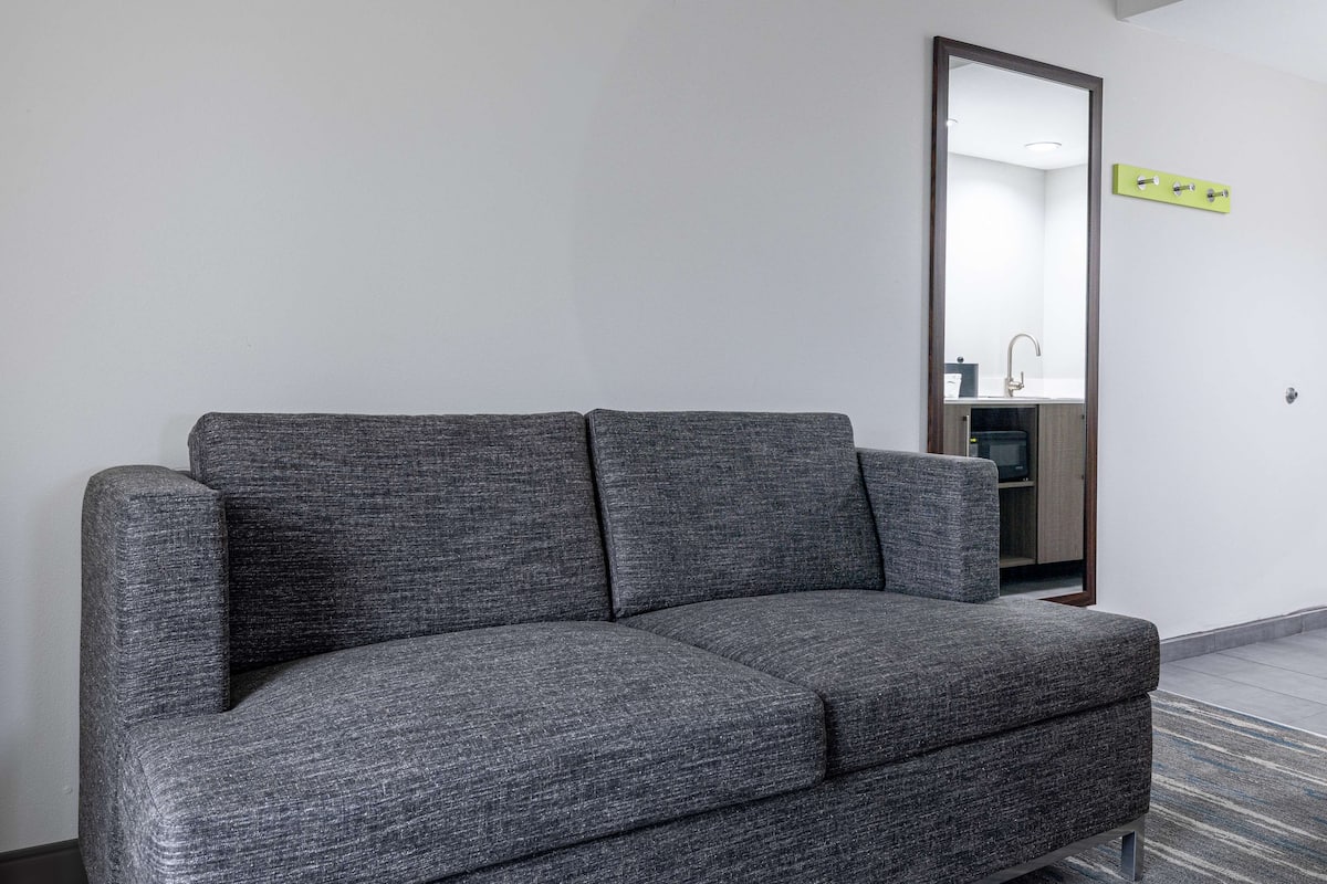 Un sofá gris en una habitación con un espejo que refleja un baño.