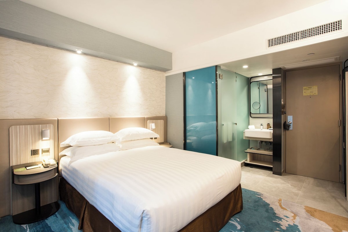 A hotel room with a large bed, bedside tables, a mirror, a wardrobe, and a bathroom with a sink and mirror.