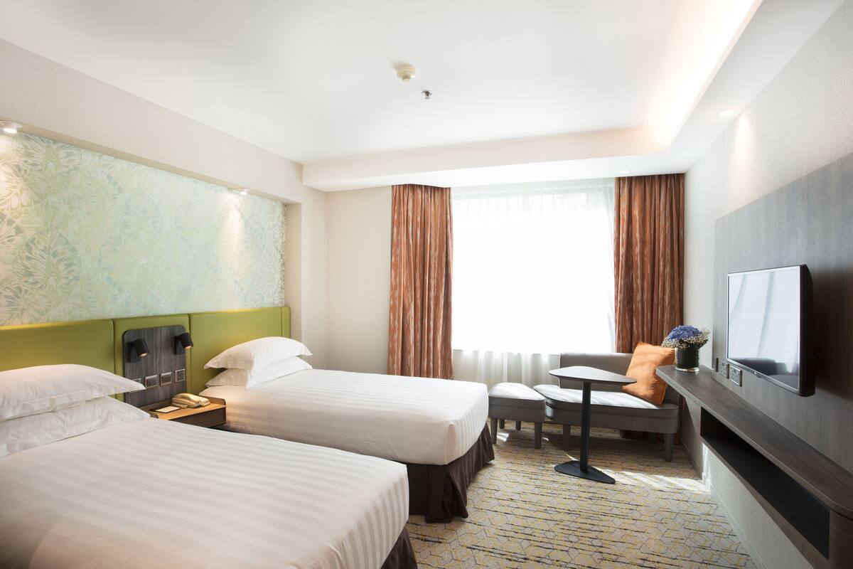 A hotel room with two beds, a desk, a chair, a TV, and a window with curtains.