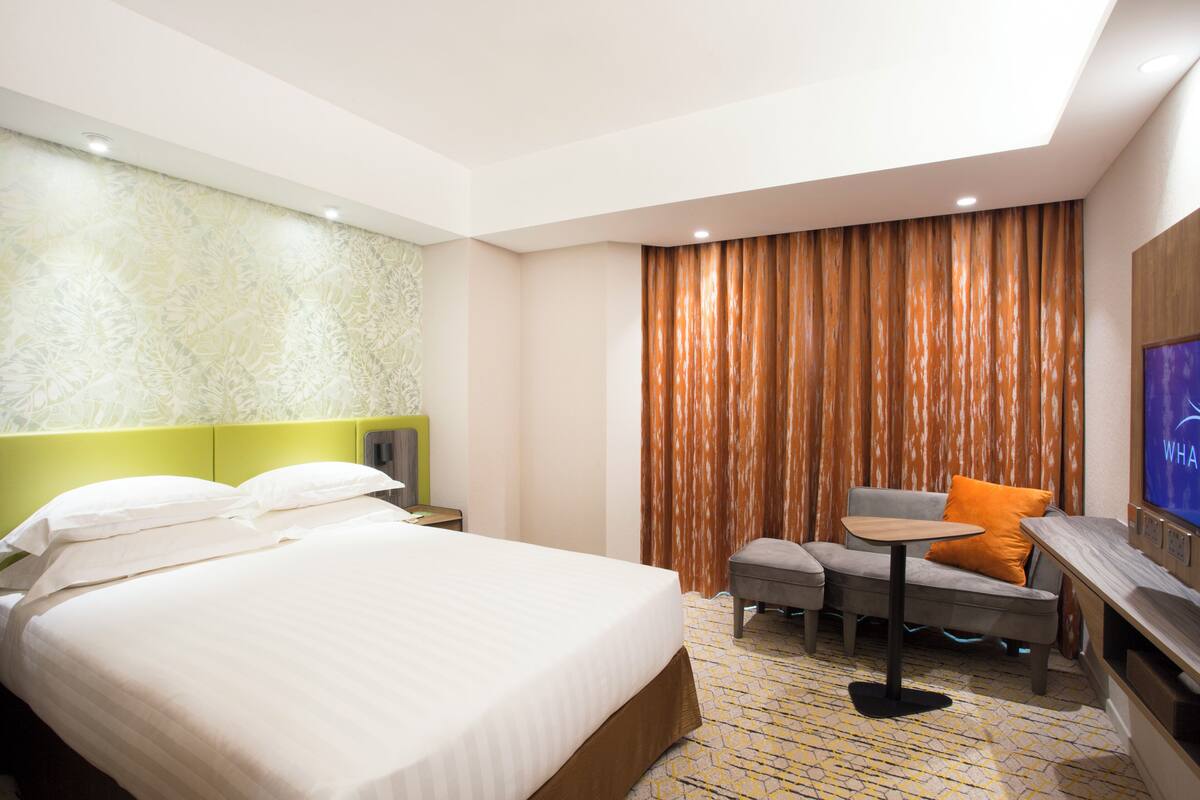 A hotel room with a large bed, a small table, a sofa, and a TV.