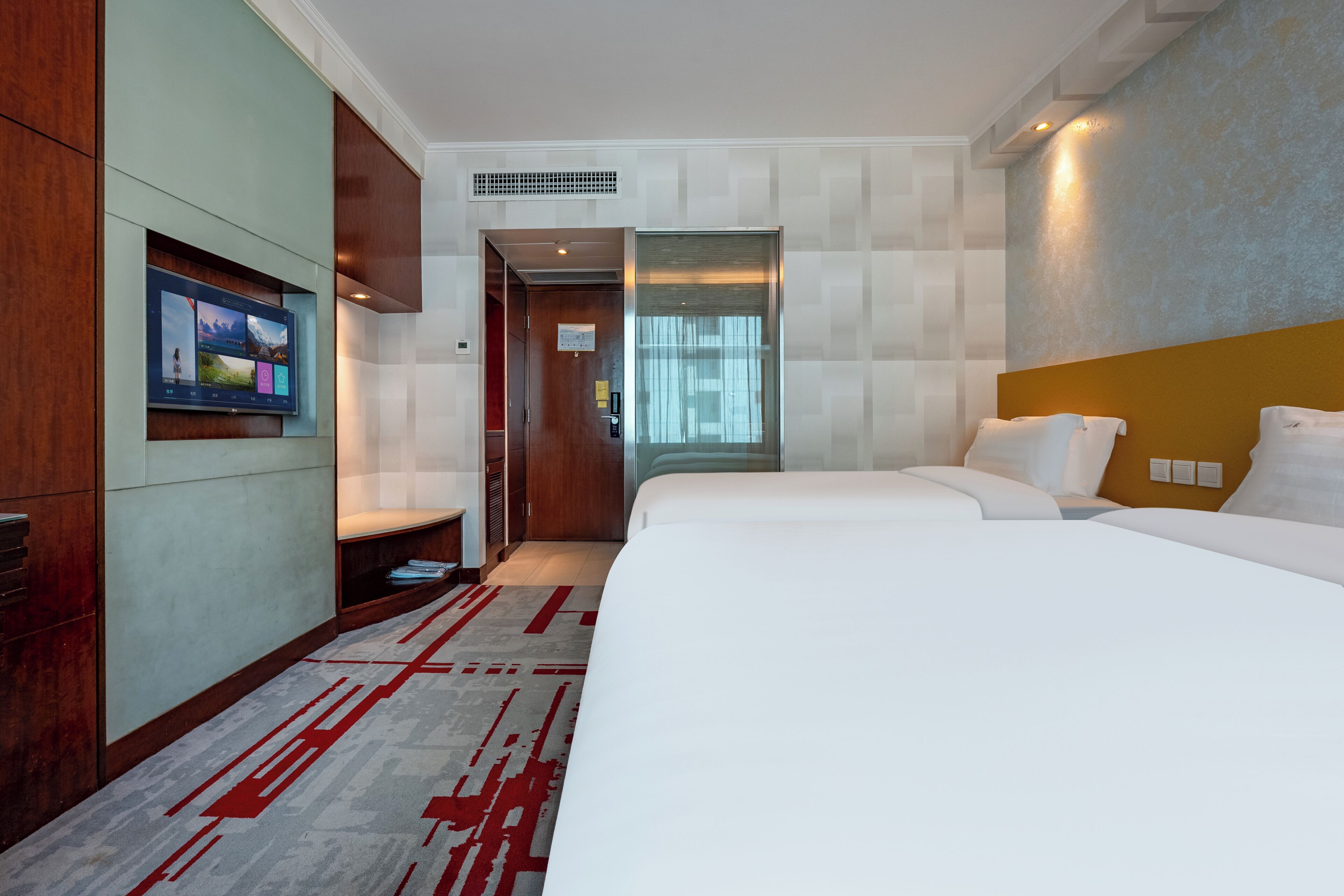 Une chambre d’hôtel avec un grand lit, un téléviseur fixé au mur et une armoire en bois.