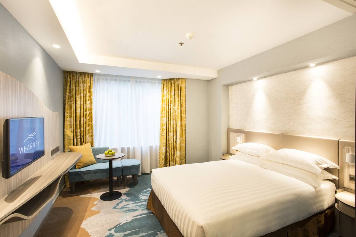 A hotel room with a bed, a TV, a desk, a chair, and a small table with fruits.