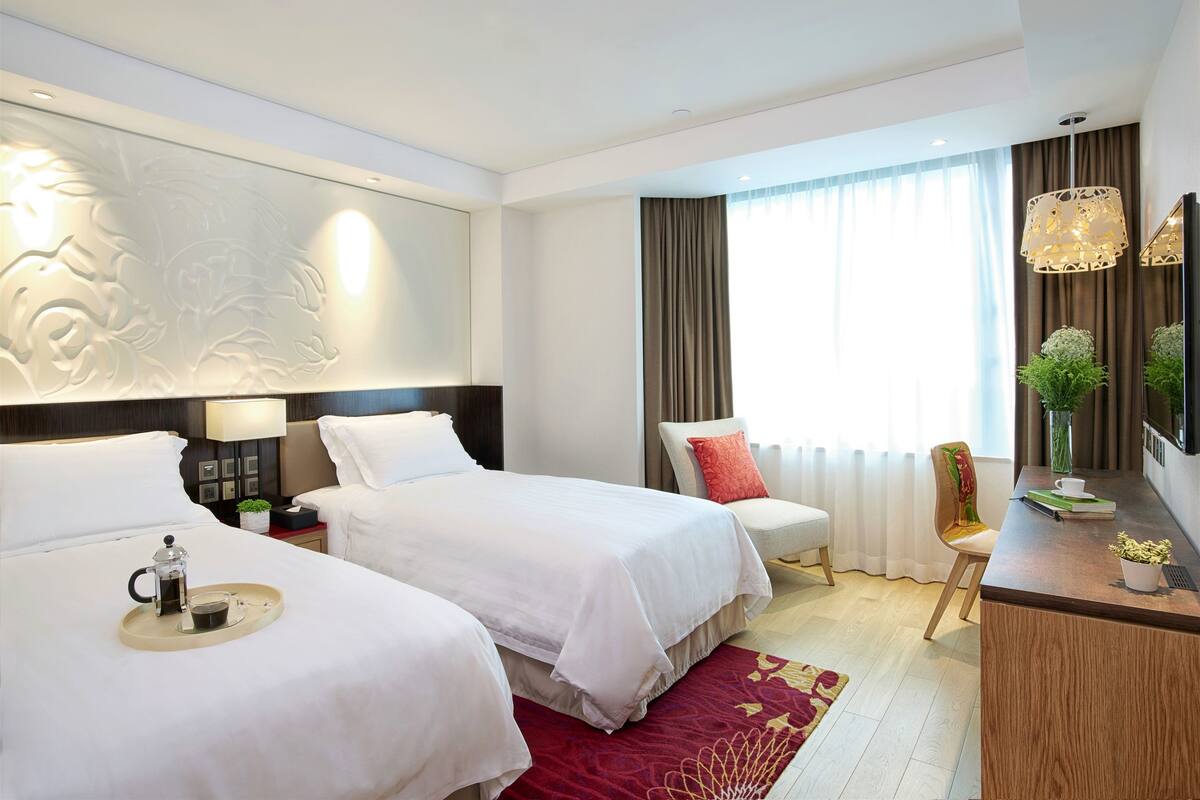 A hotel room with two beds, a desk, a chair, a coffee maker, and a decorative wall panel.