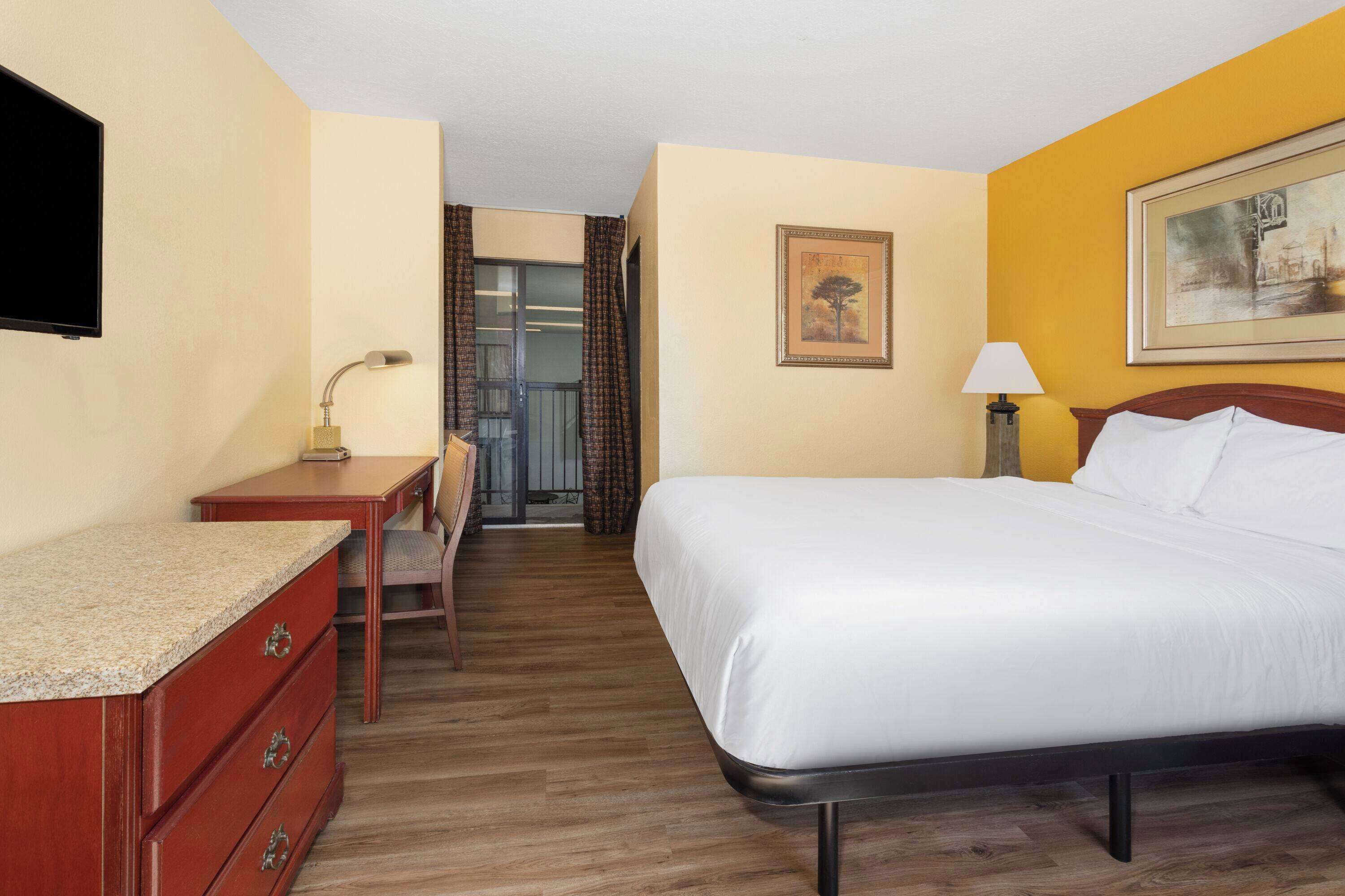 Habitación de hotel con cama, escritorio, silla, televisor y un cuadro en la pared.