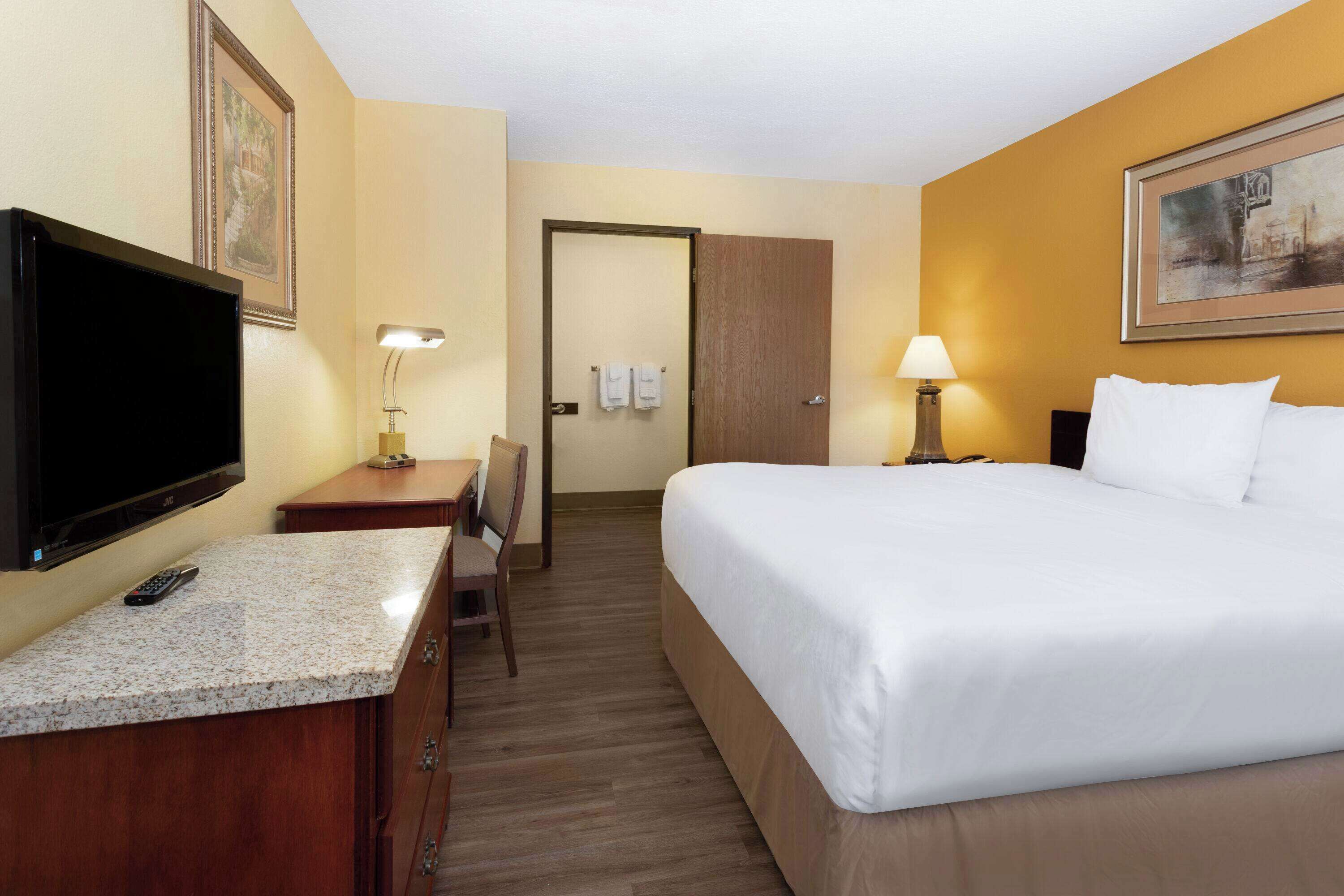 Une chambre d’hôtel avec un lit, un bureau avec une télévision, une chaise, une lampe et une porte.