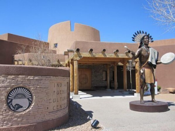 Una estatua de una figura nativoamericana frente a un edificio con la inscripción 'INDIAN PUEBLO CULTURAL CENTER'.