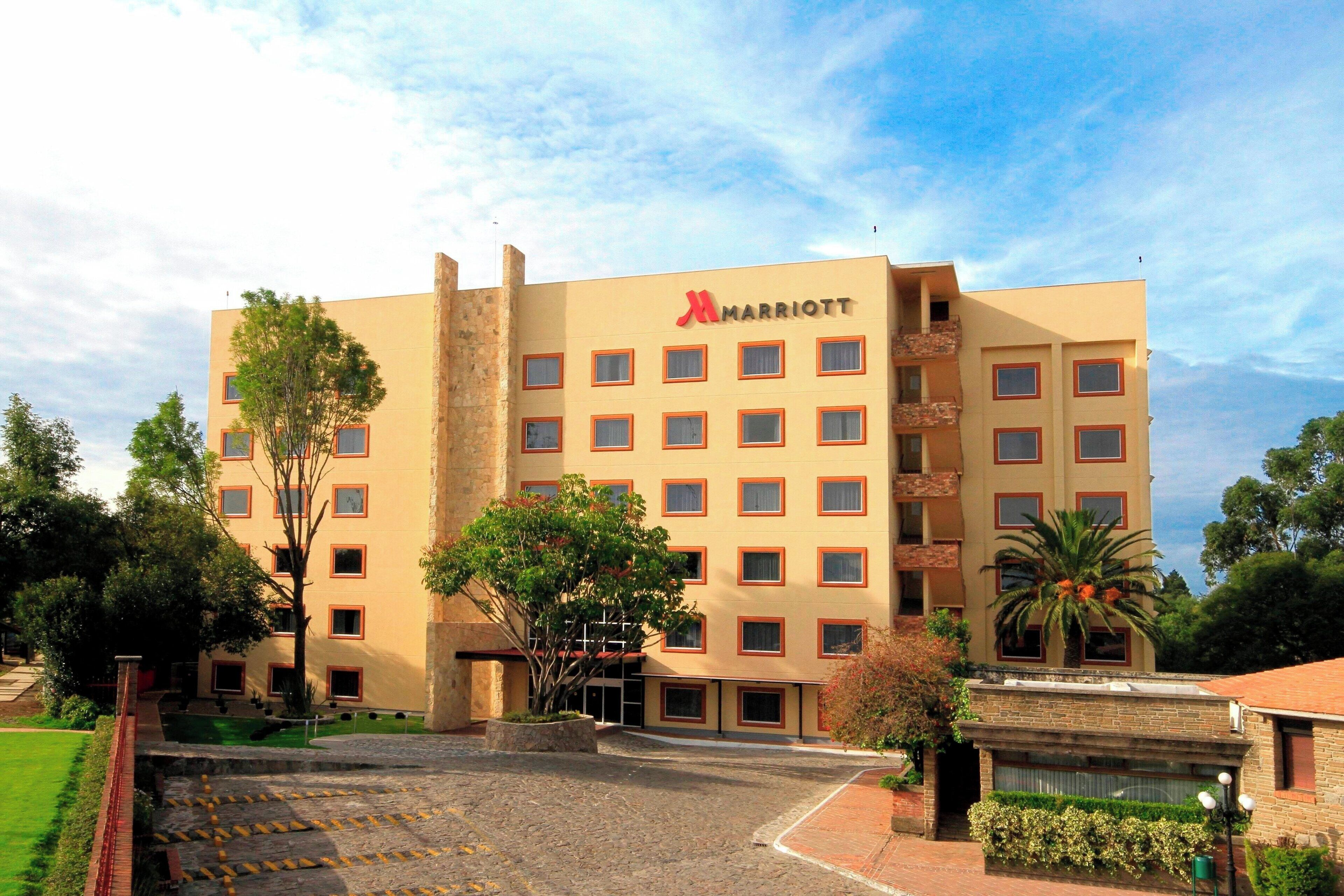 Un hôtel Marriott à plusieurs étages, doté d’une façade beige, de nombreux balcons et d’une cour aménagée.