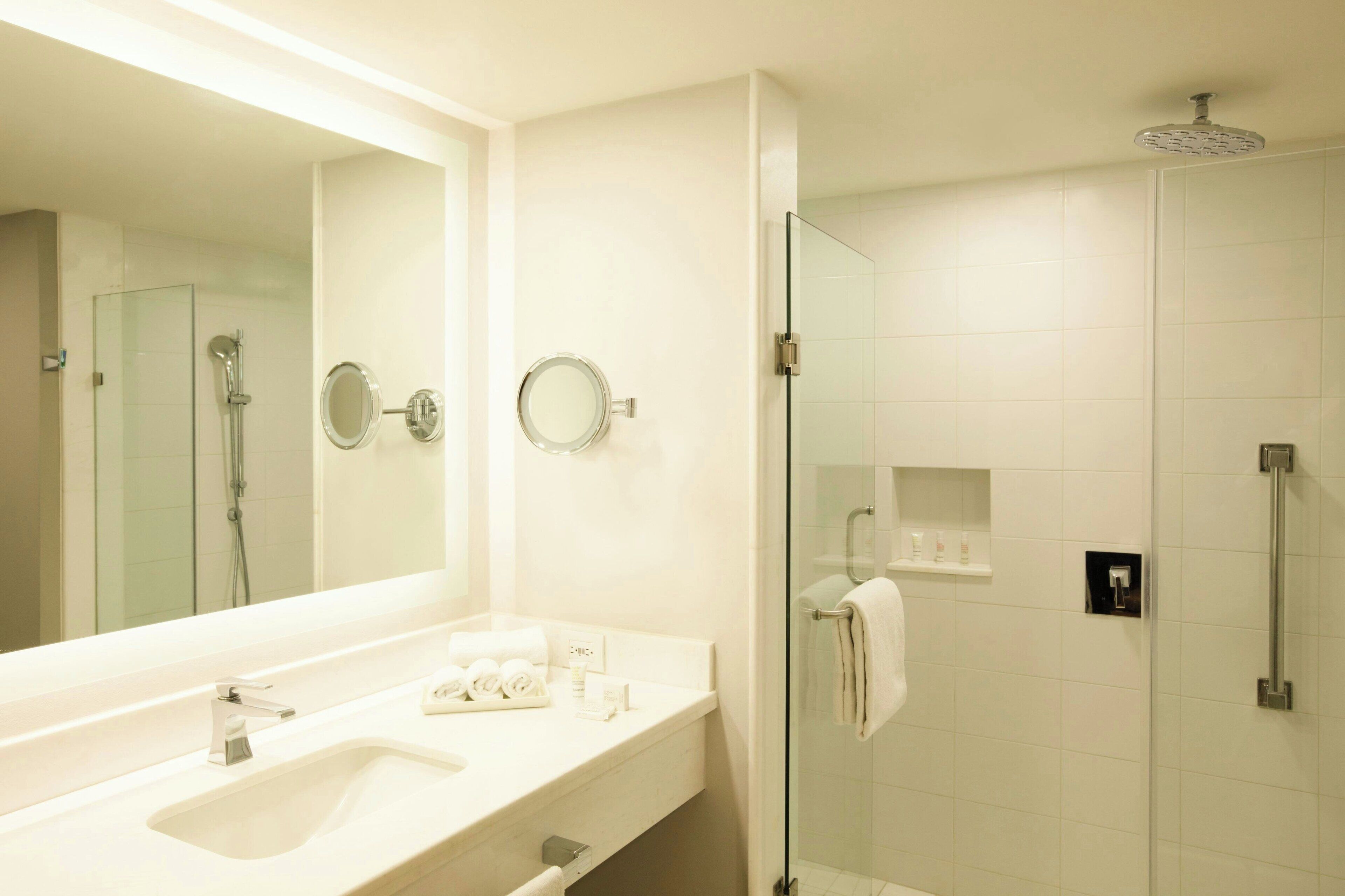 Un baño moderno con un espejo grande, un lavamanos, ducha con mampara de vidrio y un perchero para toallas.