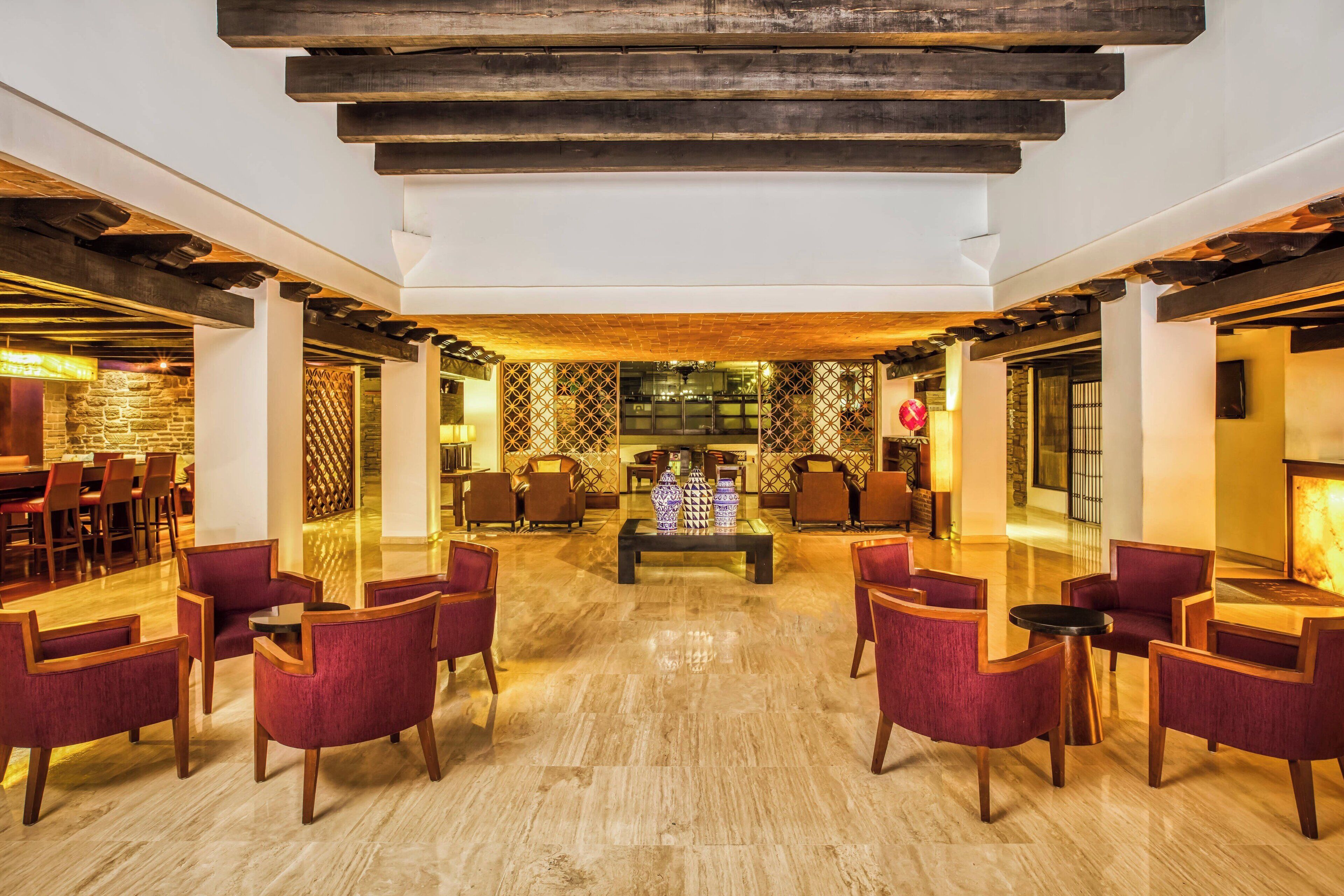 Un hall d’entrée spacieux avec des poutres en bois, une table basse centrale et des fauteuils recouverts d’un tissu rouge.