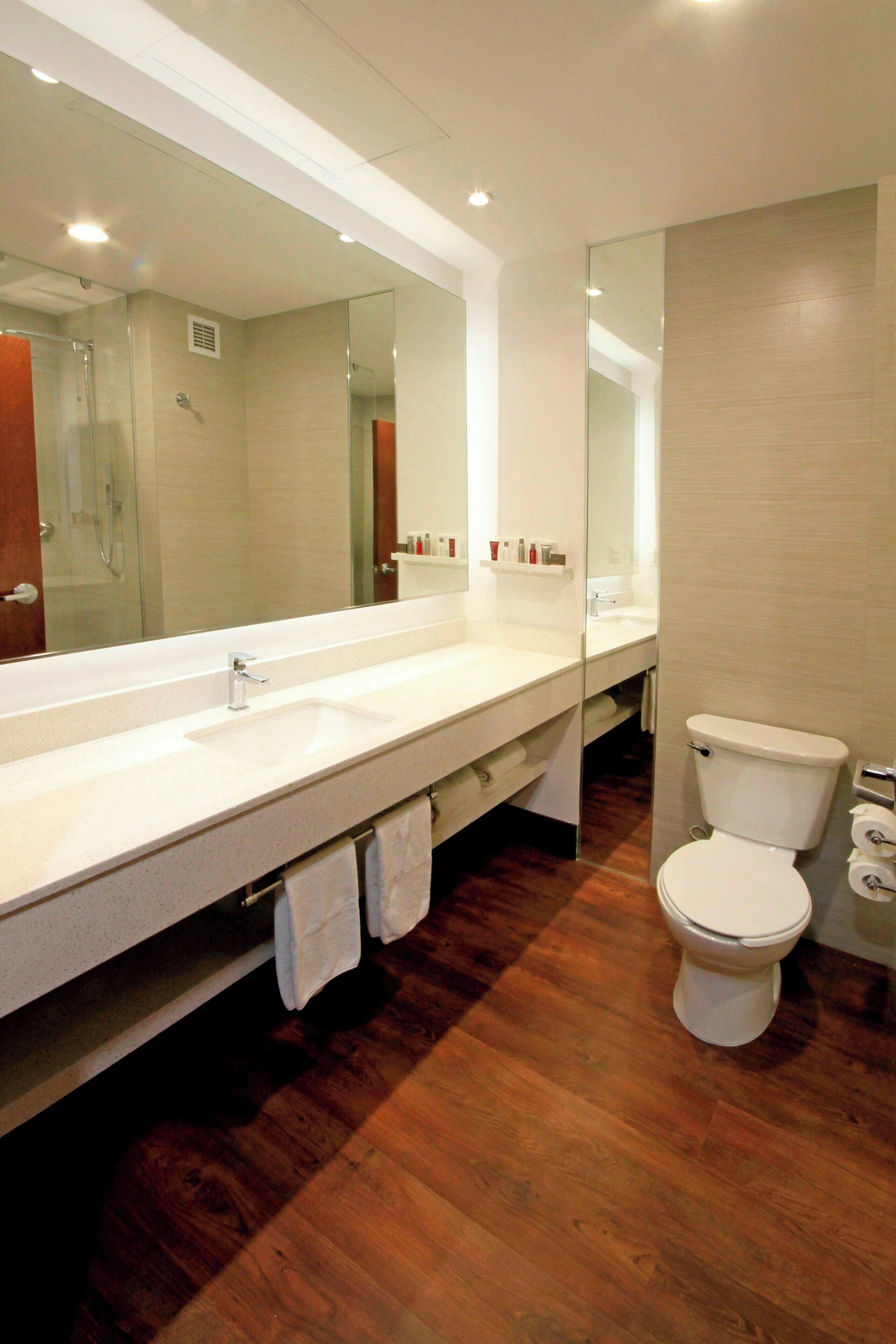 Une salle de bain moderne avec un grand miroir, un lavabo blanc, des toilettes et un revêtement de sol en bois.