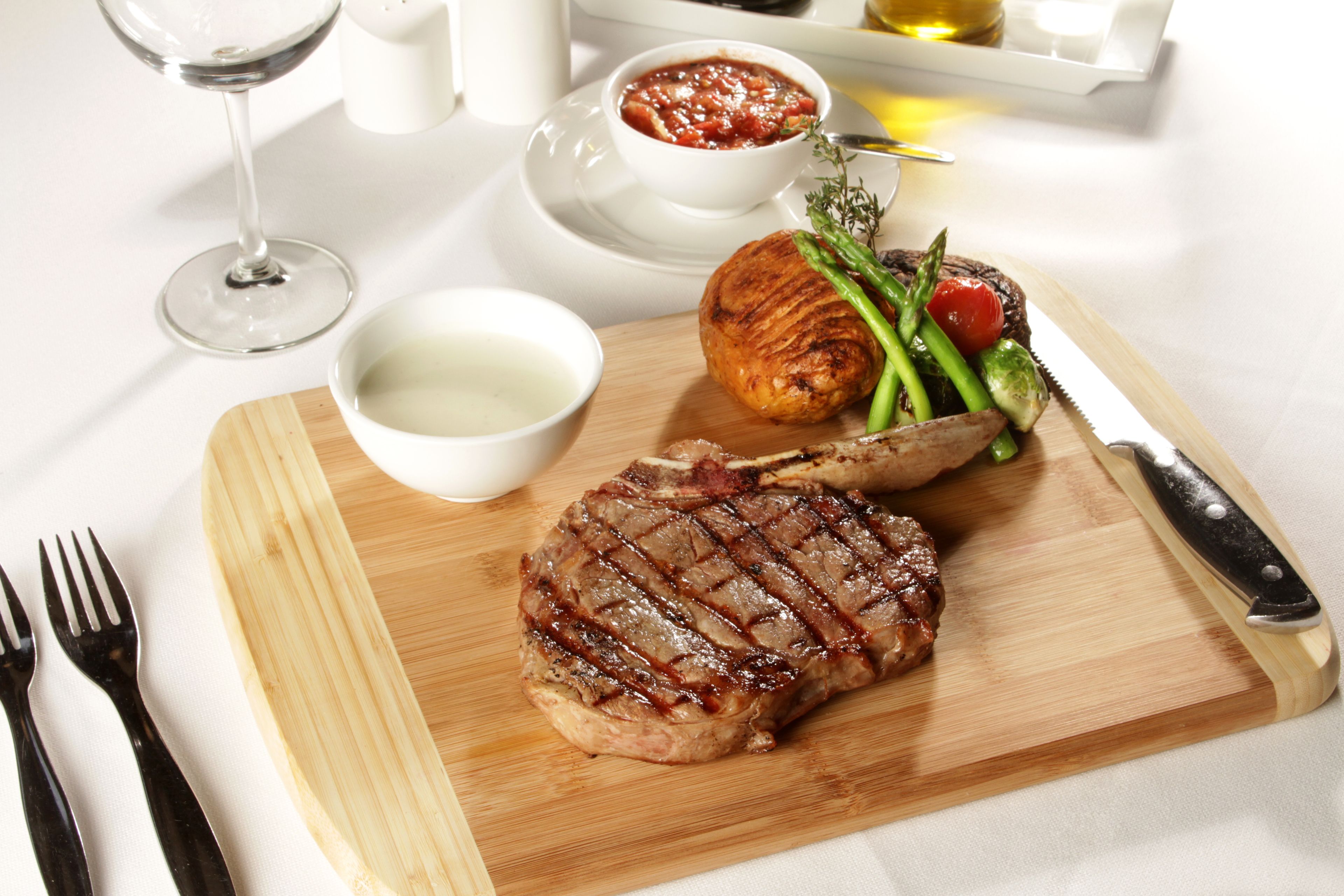 Un filete con marcas de parrilla, espárragos y una patata al horno sobre una tabla de madera.