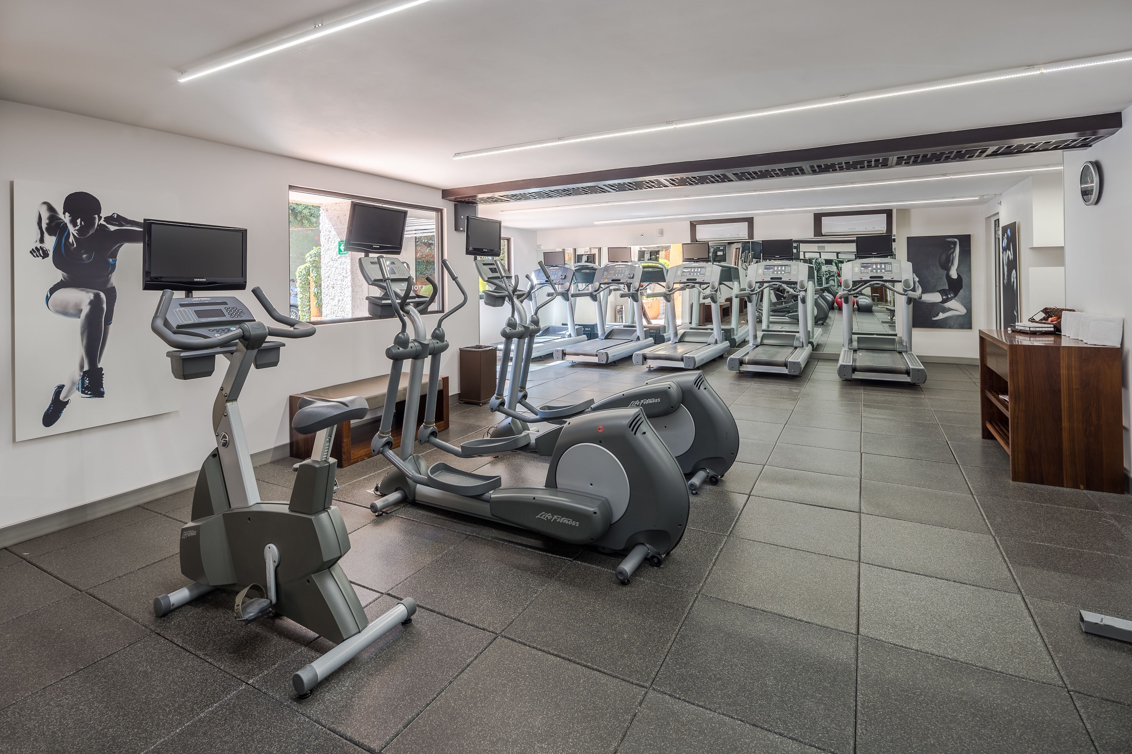 Une salle de sport équipée de tapis de course, de vélos elliptiques et d’un téléviseur fixé au mur.