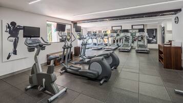 Un gimnasio con cintas de correr, elípticas y un televisor en la pared.
