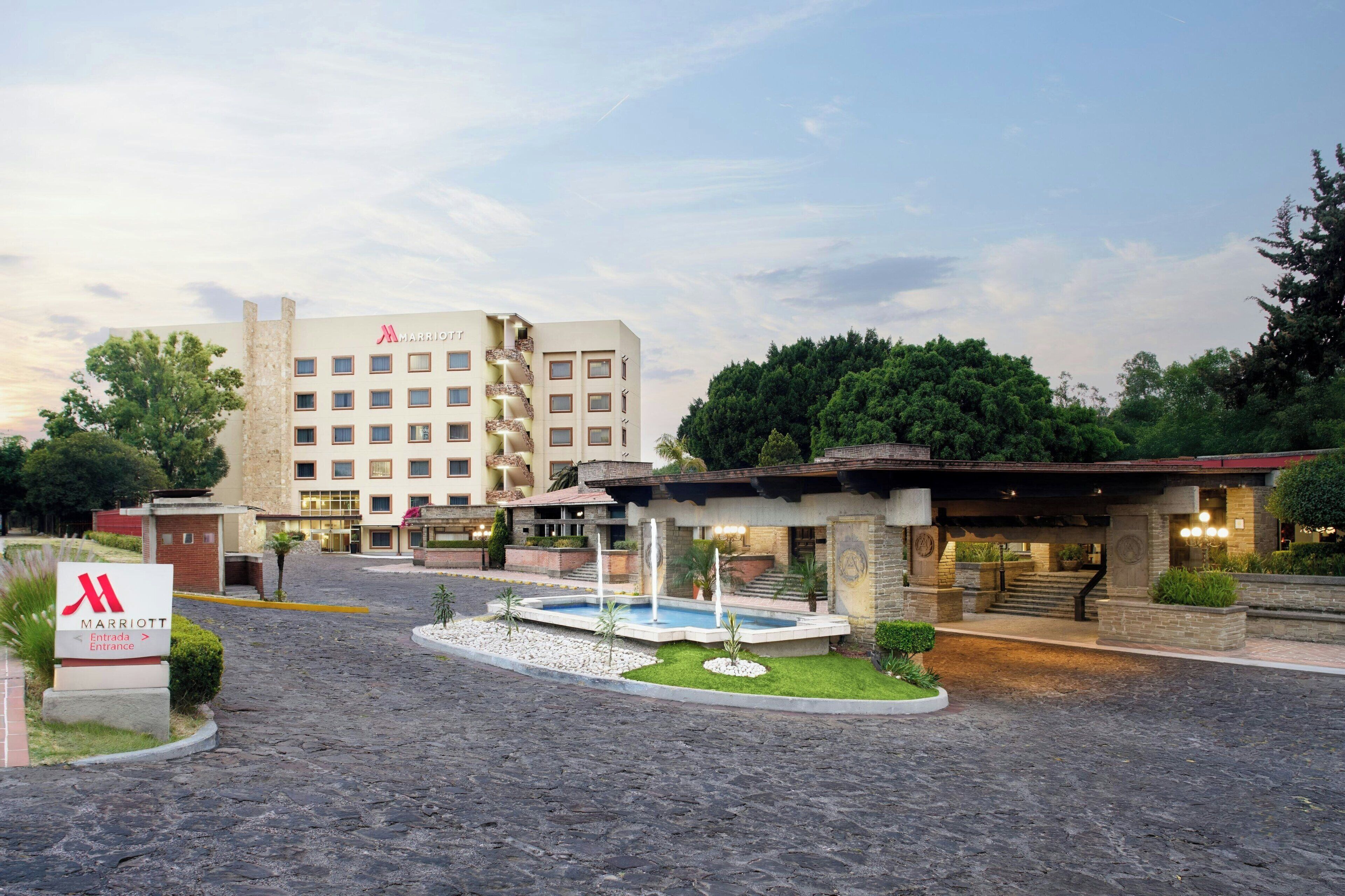 L’entrée d’un hôtel Marriott, avec une cour dallée de pierres, une piscine et un espace couvert doté d’un escalier menant au bâtiment.