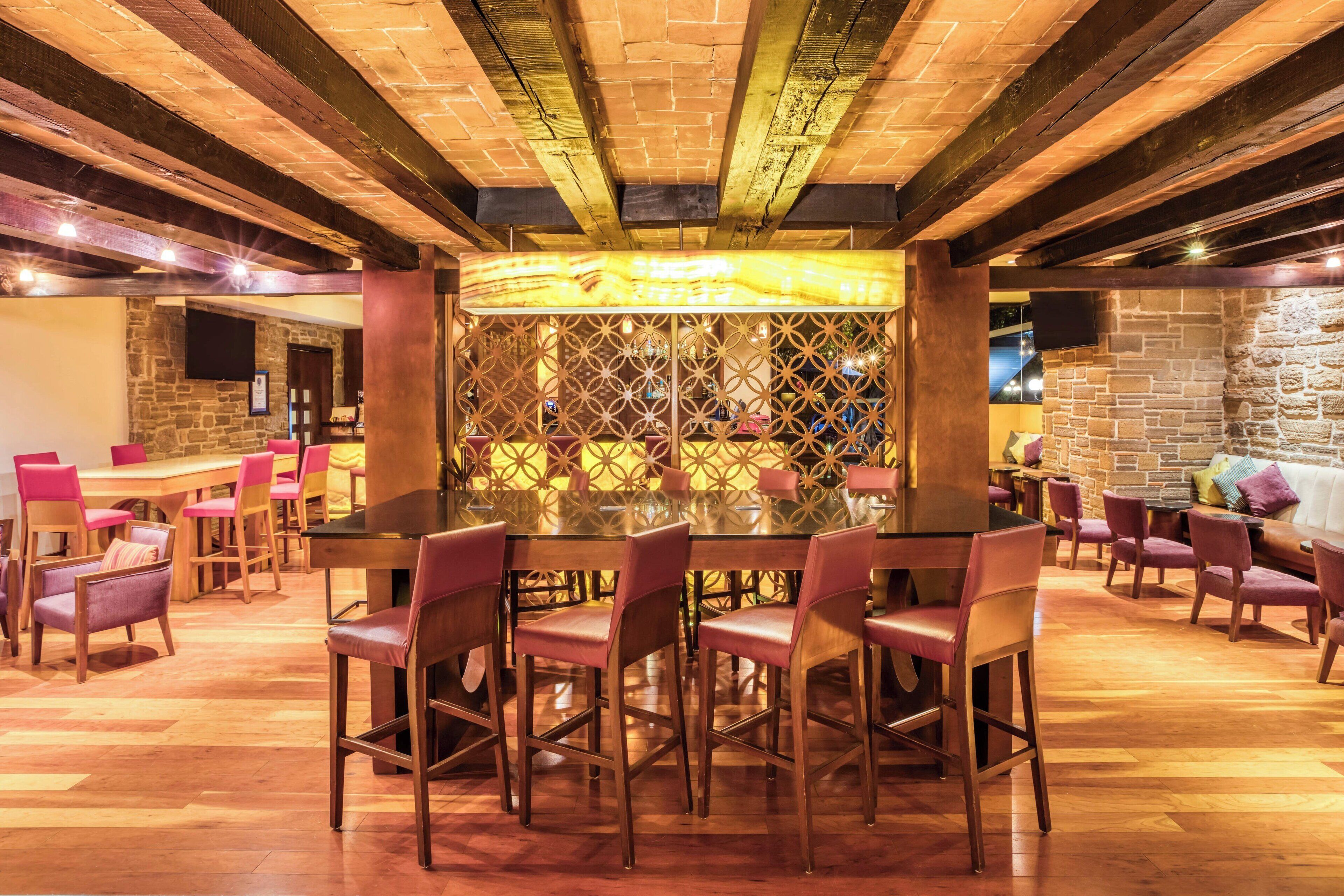 A restaurant with a central dining table surrounded by chairs, wooden flooring, and a stone wall with a decorative screen in the background.