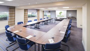 Un salón de conferencias con una larga mesa, sillas azules y una pantalla mostrando el logotipo de Holiday Inn.