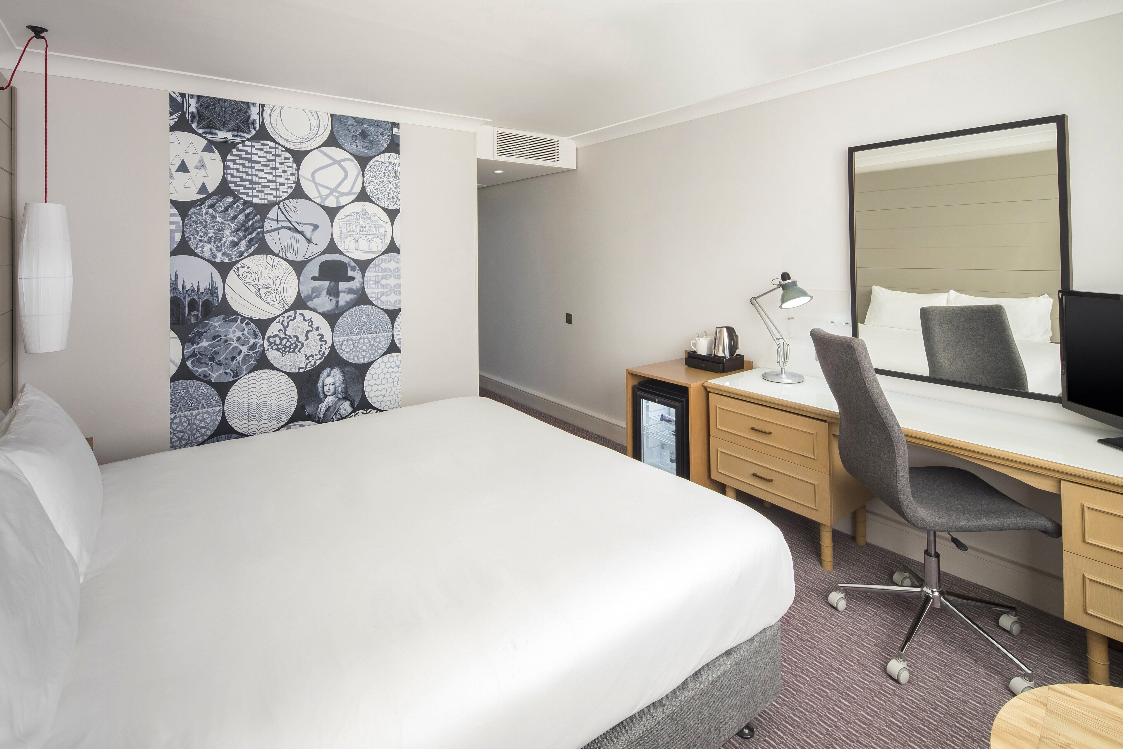 Ein Hotelzimmer mit einem großen Bett, einem Schreibtisch mit Stuhl, einem Computer und einem Spiegel.