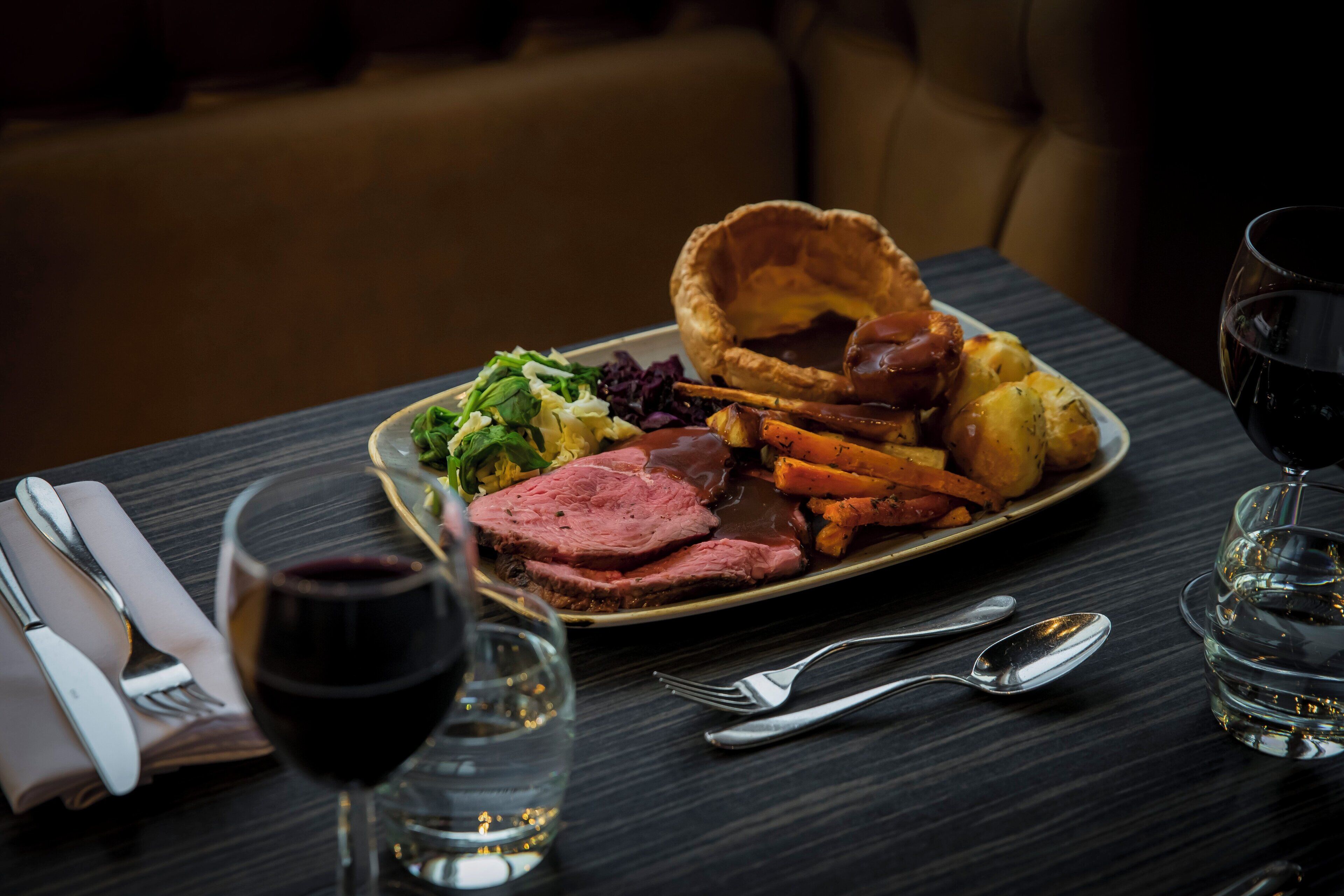 A dining table with a plate of food, a glass of red wine, and cutlery.