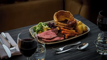 A dining table with a plate of food, a glass of red wine, and cutlery.