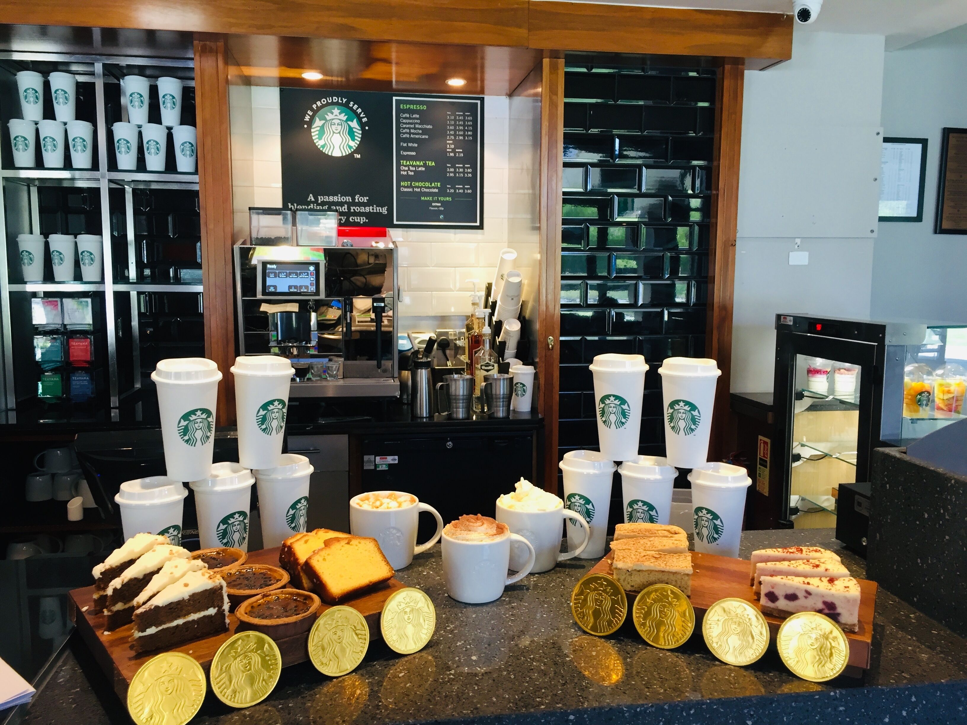 A Starbucks coffee shop counter with various coffee cups, pastries, and Starbucks-branded items.