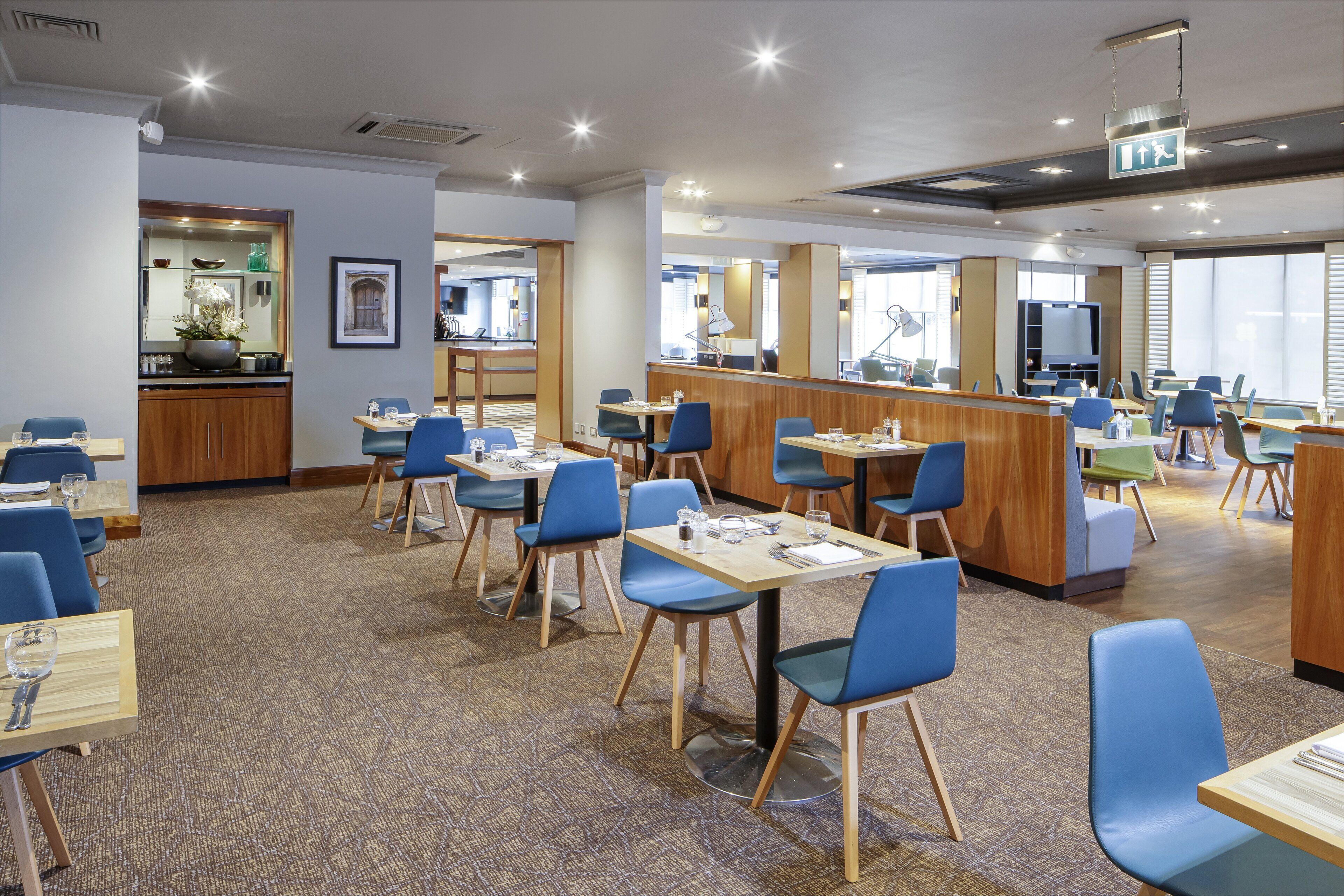 Une salle à manger d’hôtel avec plusieurs tables et chaises, un comptoir agrémenté d’un miroir et donnant sur la pièce adjacente.
