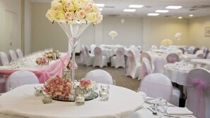 Une salle de banquet avec des tables rondes dressées pour un événement formel, agrémentée de compositions florales et de nappes blanches.