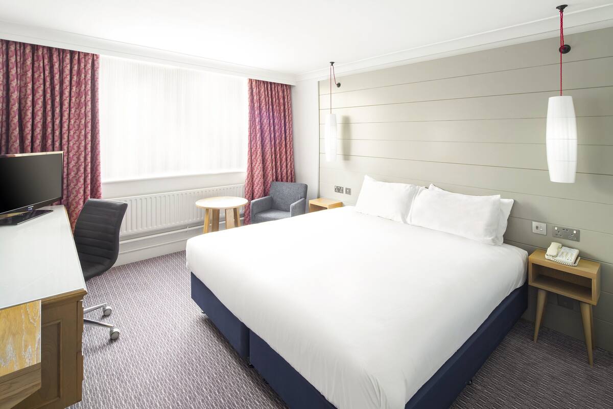 Une chambre d’hôtel avec un grand lit, un bureau avec un ordinateur, une chaise, une petite table et un téléphone sur une table de chevet.