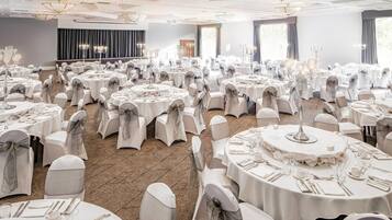 A banquet hall with round tables set for dining, each with white tablecloths and silverware.