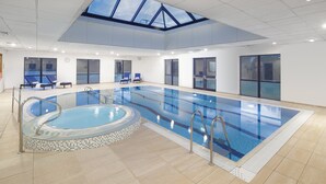 Une piscine intérieure dotée d’une verrière, de chaises longues et d’un jacuzzi.