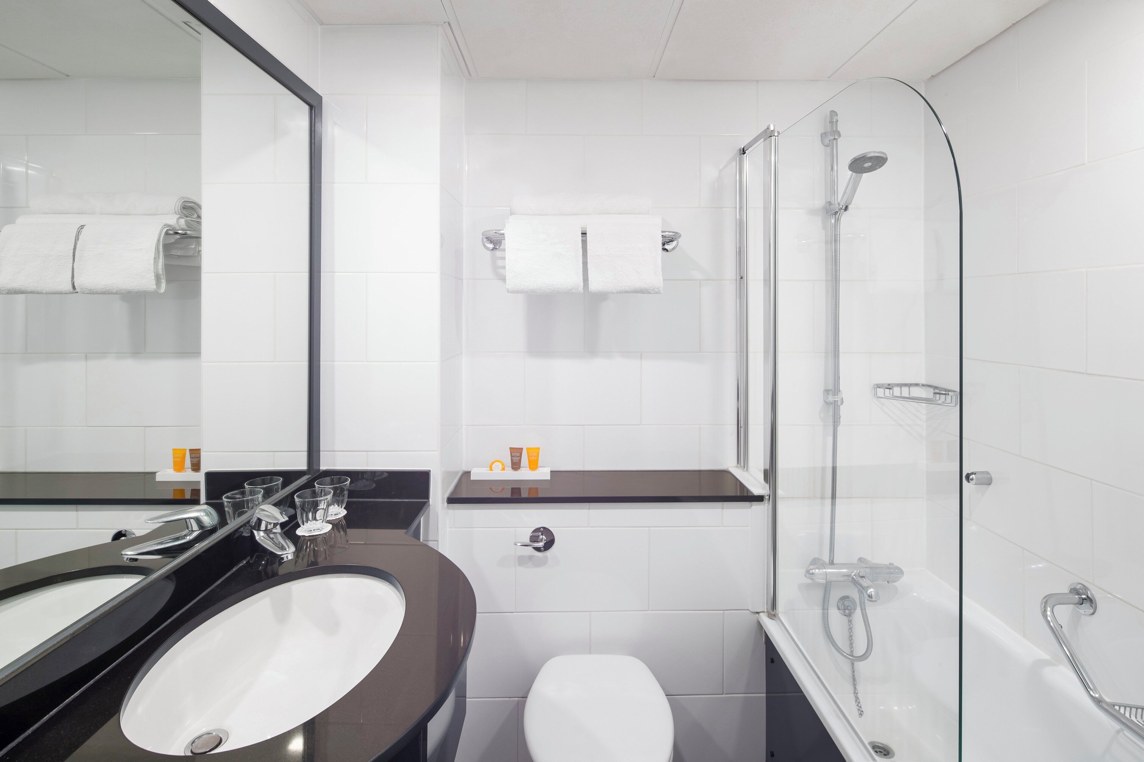 A modern bathroom with a large mirror, a sink, a toilet, and a glass-enclosed shower area.