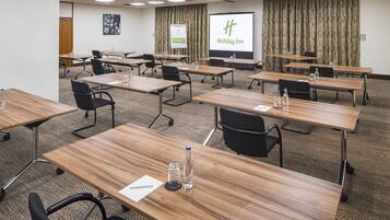 A conference room with multiple tables, chairs, and a large screen displaying the Holiday Inn logo.