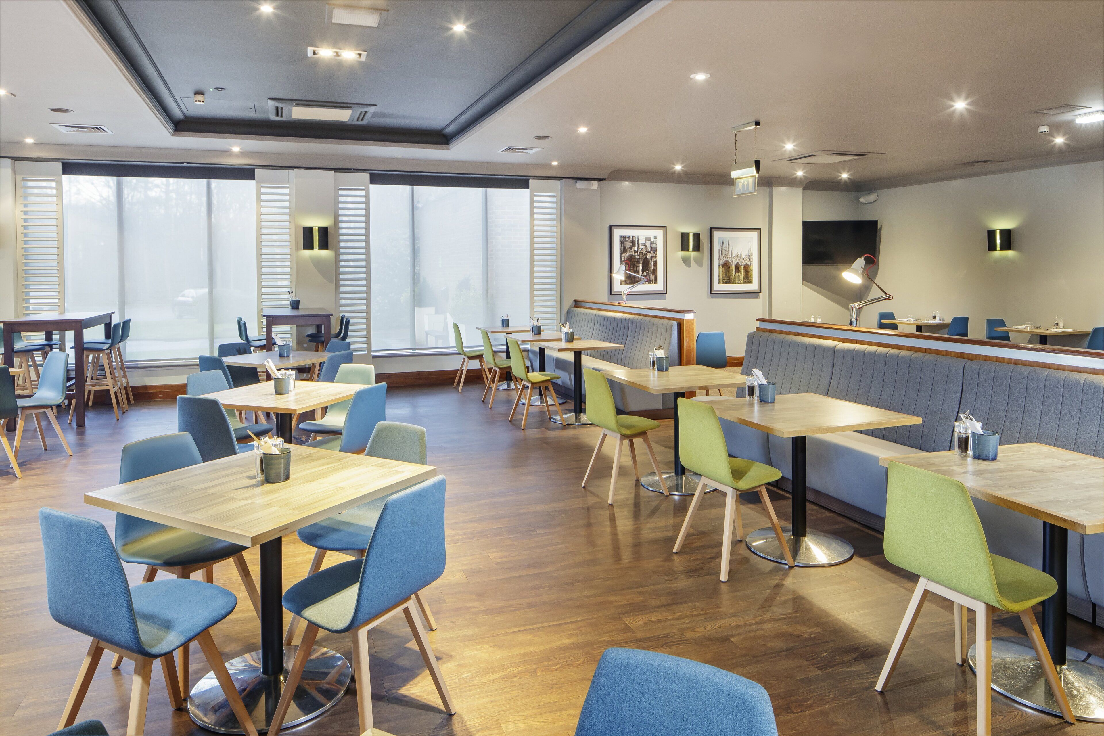 Un espace repas moderne avec des tables et des chaises en bois, de grandes fenêtres et des œuvres d’art accrochées aux murs.