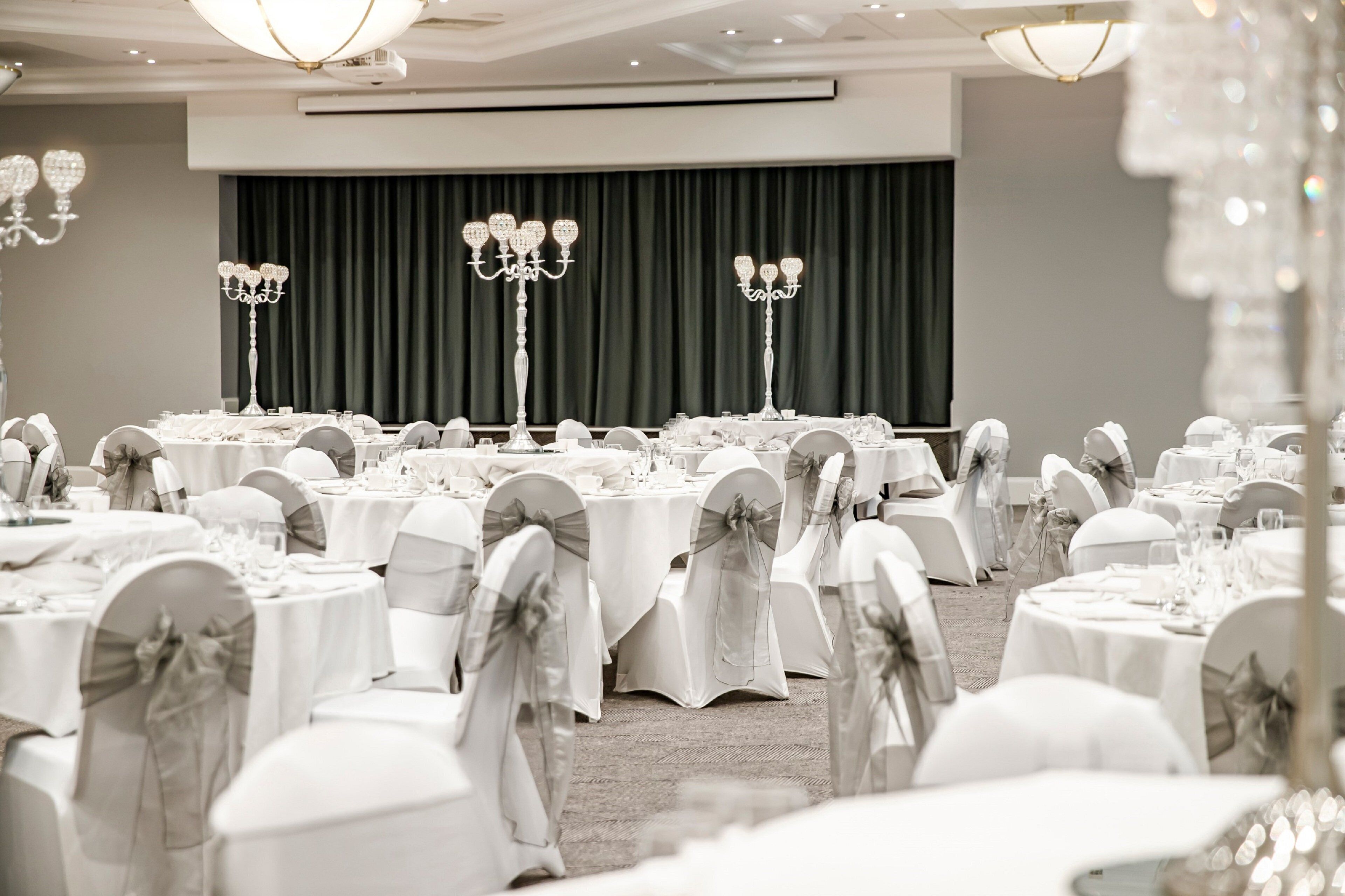 A banquet hall with round tables, white tablecloths, and chairs with bows.