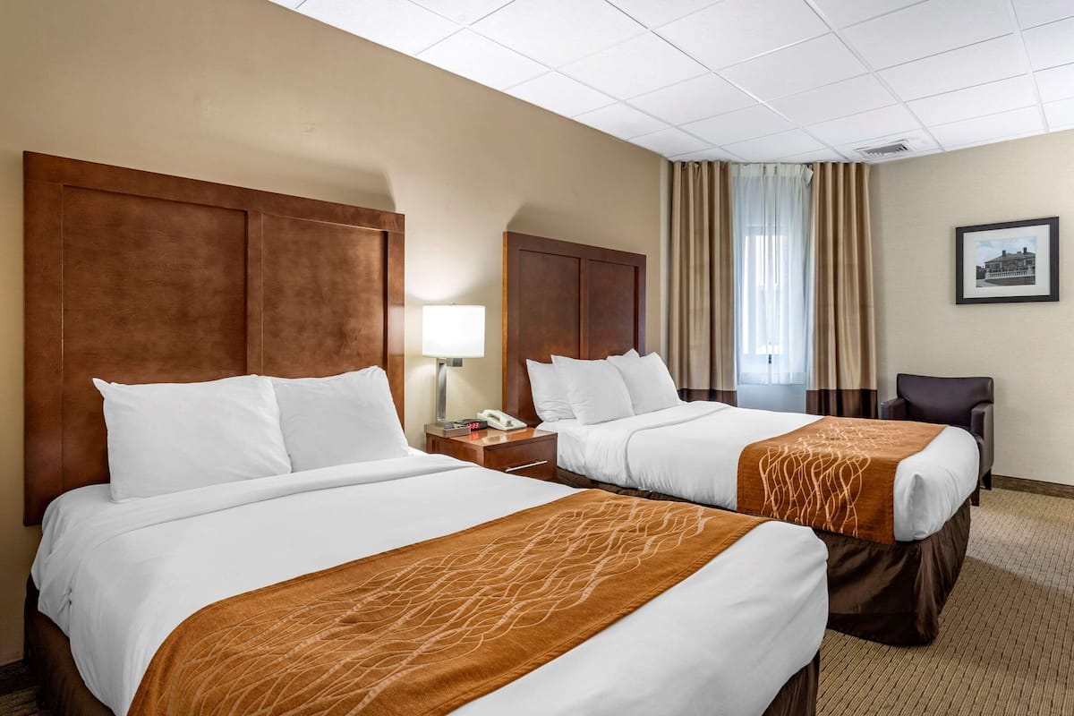 A hotel room with two beds, a nightstand with a lamp, a chair, and a framed picture on the wall.