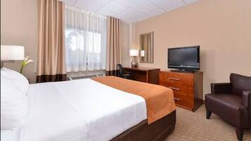 A hotel room with a large bed, a desk with a computer, a television, and a chair.