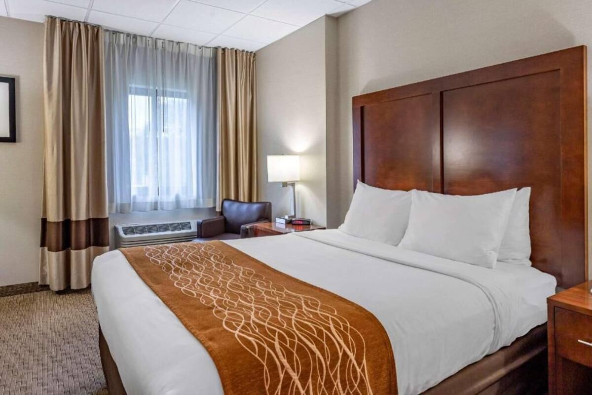 A hotel room with a large bed, a desk, a chair, a lamp, and a window with curtains.