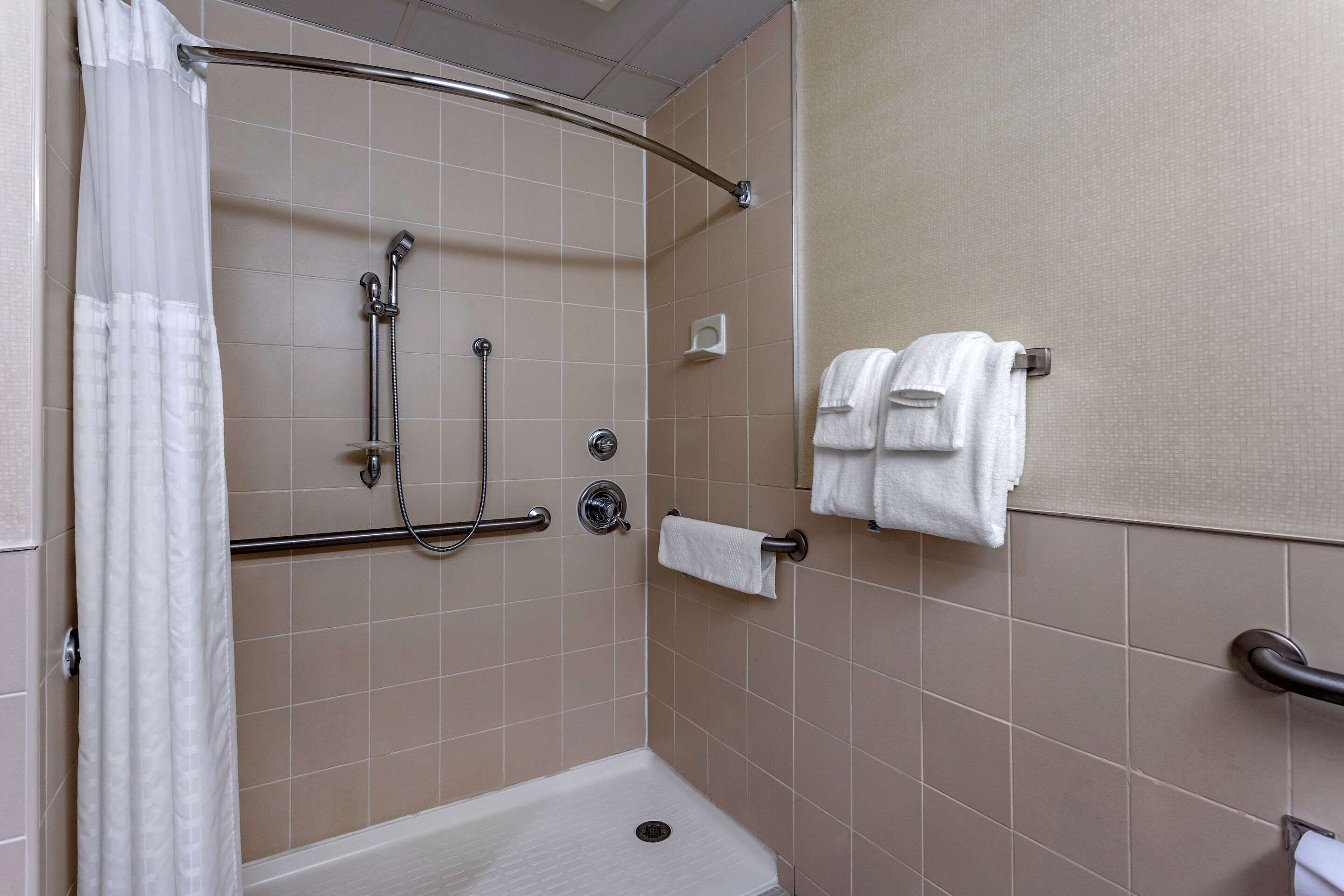 A shower area with a grab bar, a towel rack with two towels, and a shower curtain.