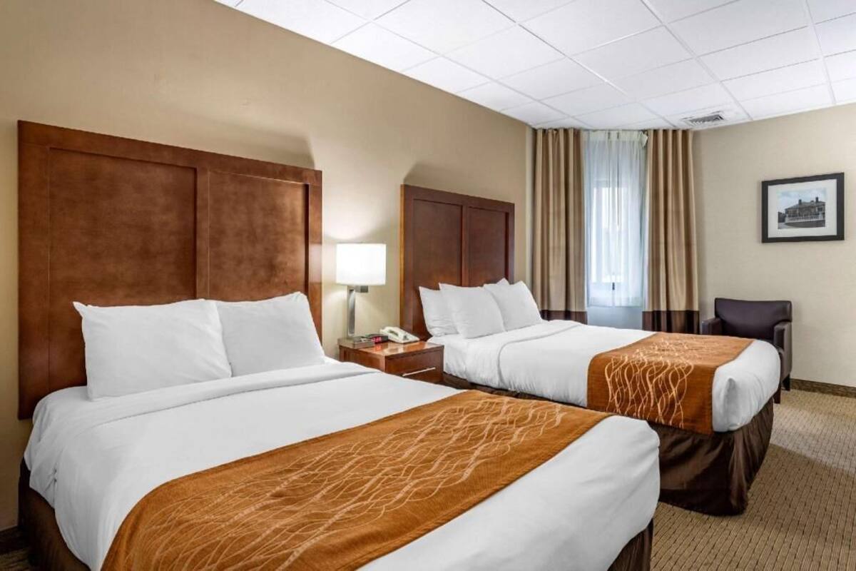 A hotel room with two beds, a desk, a chair, a lamp, and a framed picture on the wall.