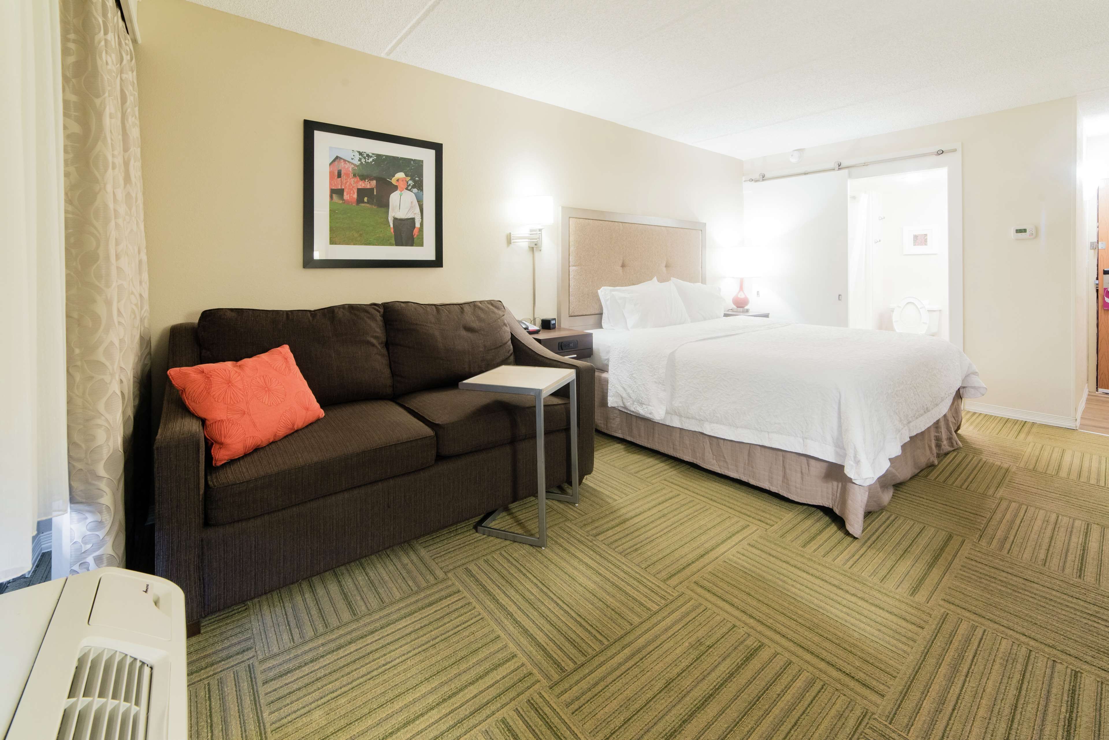 A hotel room with a bed, a sofa, a small table, and a picture on the wall.