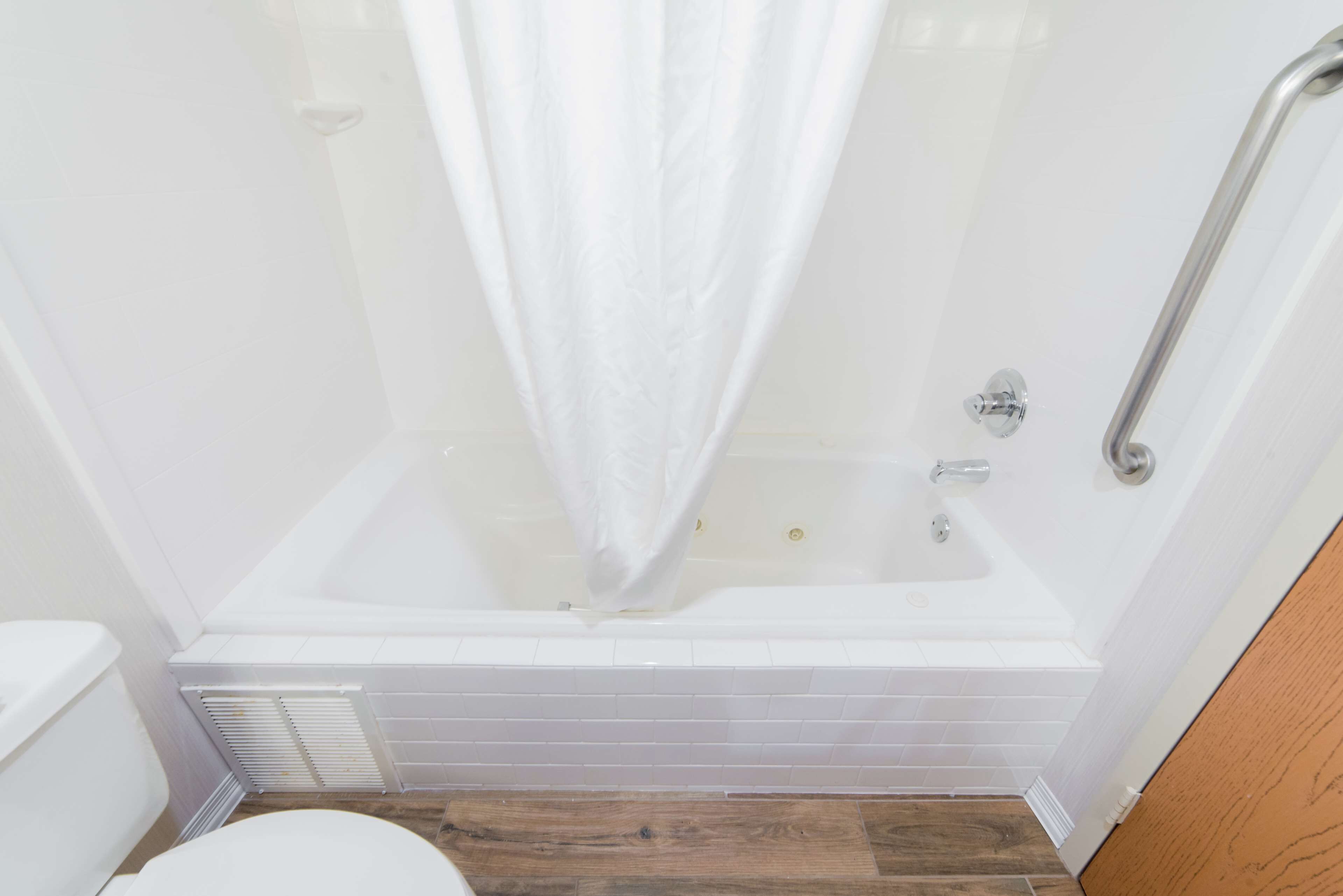 Un baño con una bañera blanca, una cortina de ducha y suelo de madera.
