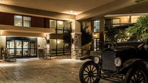 Fachada de un edificio con un coche antiguo estacionado frente a él, pilares de piedra y un camino empedrado.